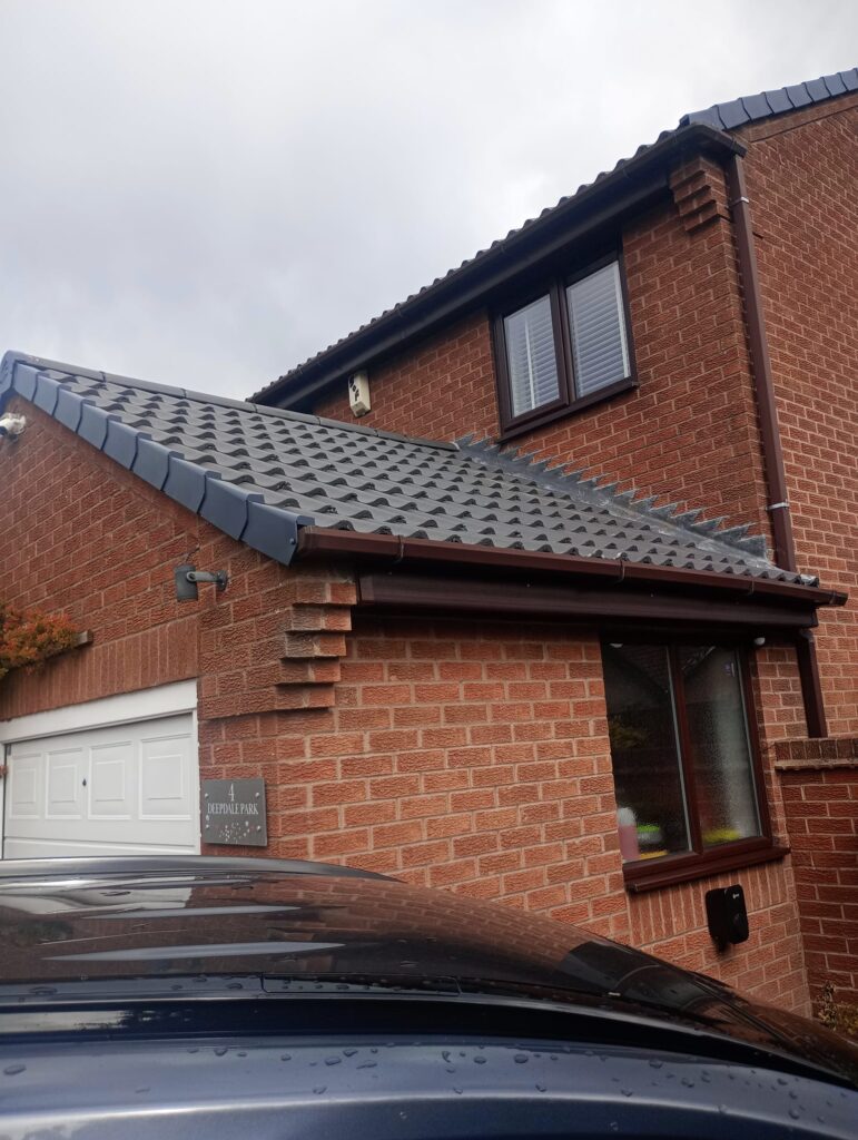 Roofline Upgrades 3 Newly installed dark grey roof tiles and brown gutters on a modern brick house, showcasing roofline upgrades by checka roof ltd in london.