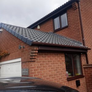 Roofline Upgrades 8 Newly installed dark grey roof tiles and brown gutters on a modern brick house, showcasing roofline upgrades by checka roof ltd in london.